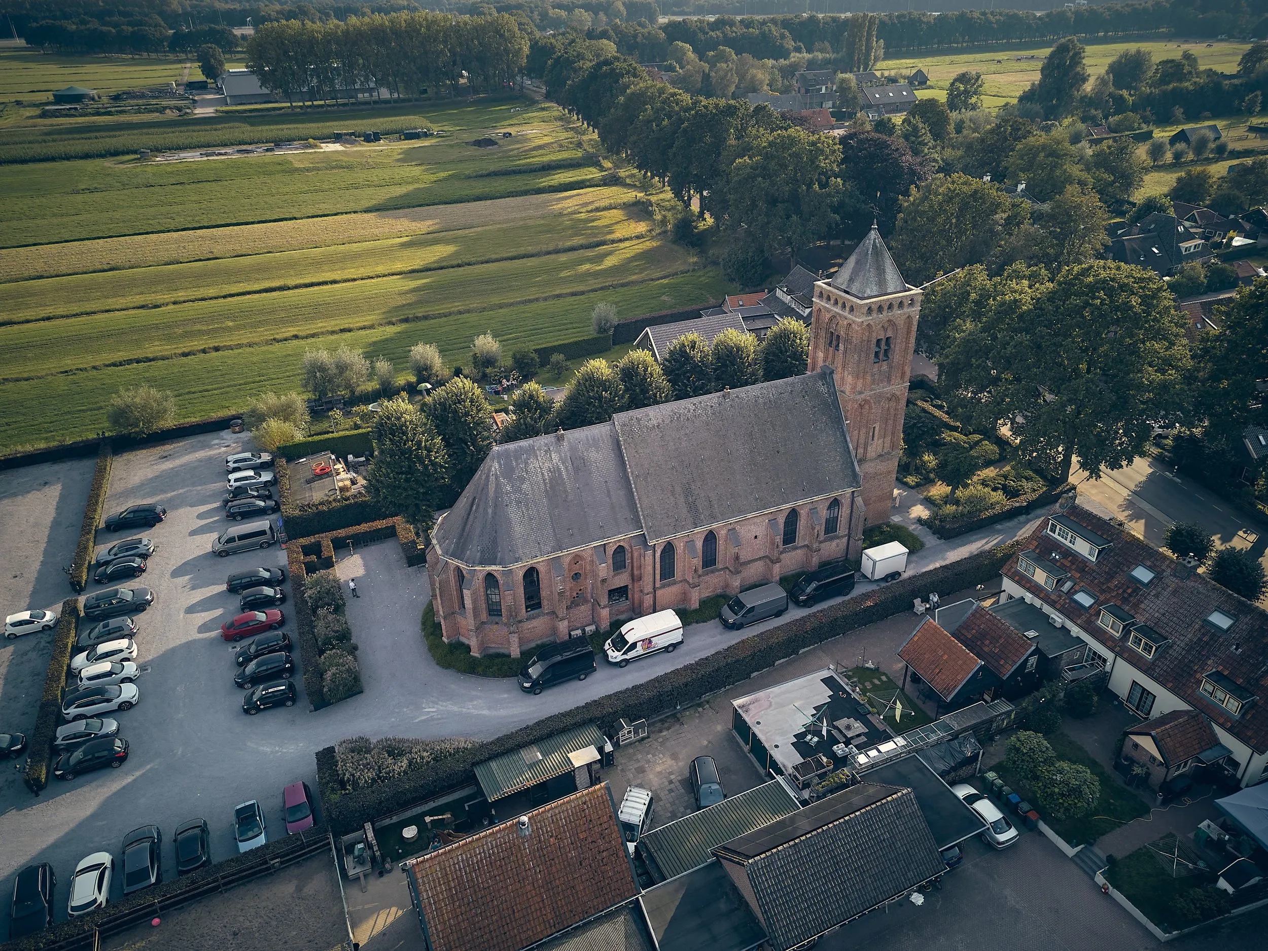 Luchtfoto van de pittoreske kerk Het Dikke Torentje omringd door landelijke weilanden en parkeerplaats
