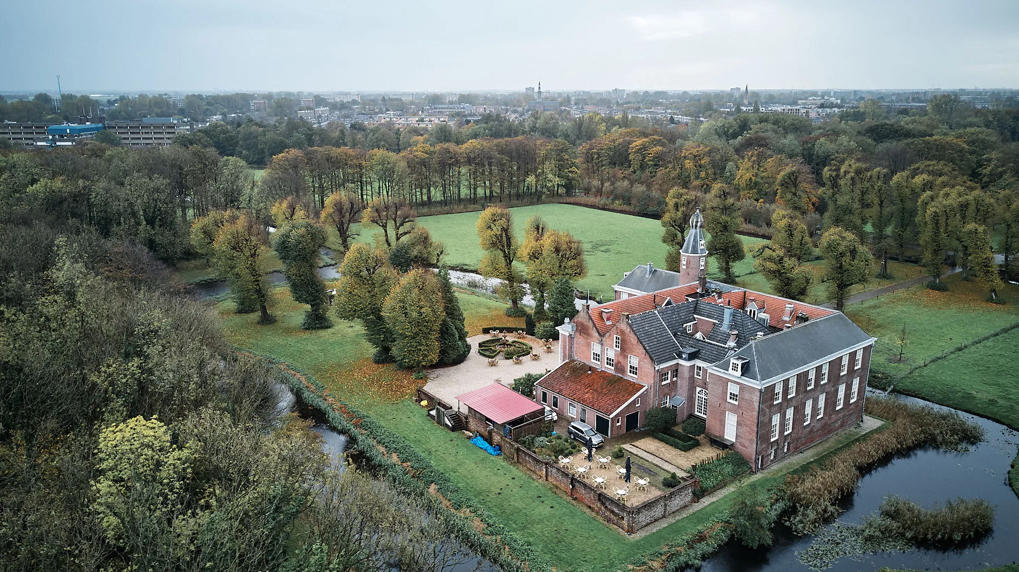 Landhuisje omgeven door weilanden en bos in herfstsfeer, gezien vanuit de drone