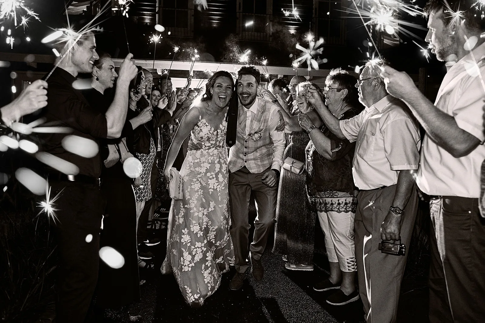 Bruidspaar dansen door sprankelende sterretjes bij feestelijk trouwfeest 's avonds, gasten zwaaien met lichtjes, trouwreporta