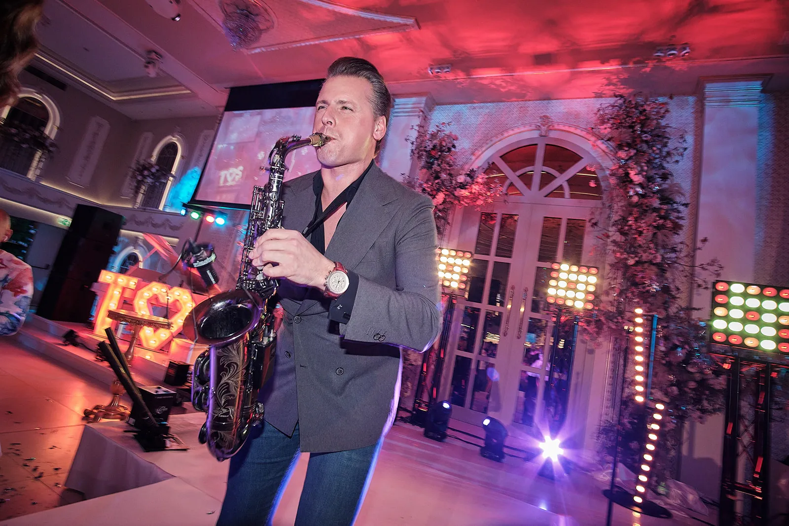 Saxofonist speelt tijdens bruidsfestijn met roze en blauwe verlichting, feestelijke trouwreportage