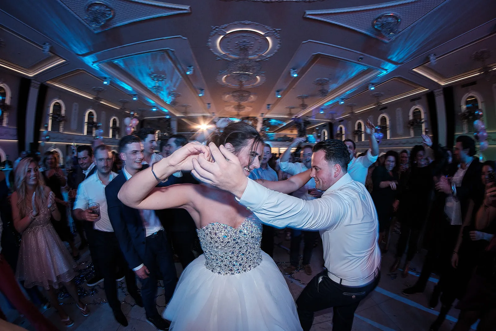 Bruidspaar danst samen op bruidsfeest in elegant verlichte zaal, gasten juichen toe, romantische trouwreportage