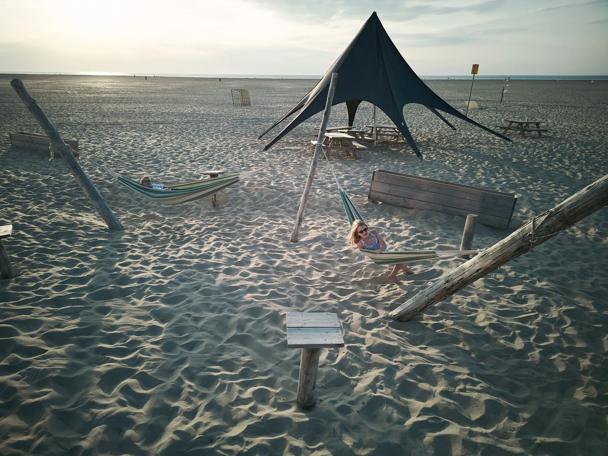 Mirjam en Jorg relaxen in hangmatten onder een zwarte strandtent met uitzicht op zee in Strandpaviljoen Brouw