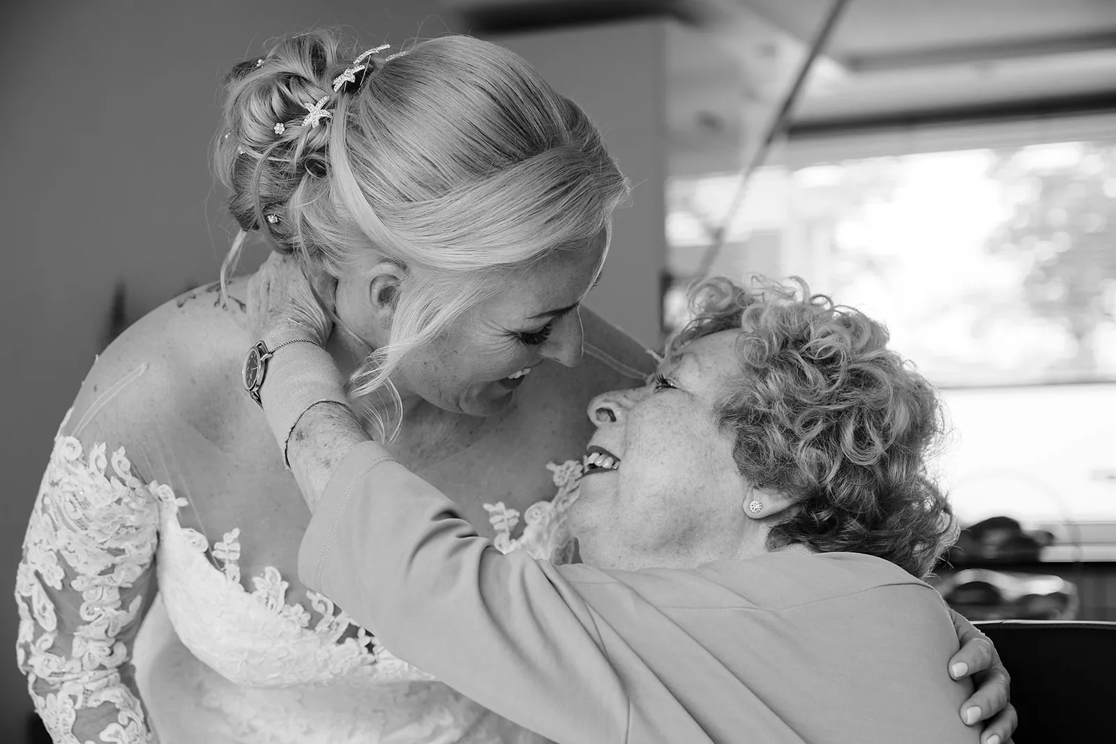 Bruid in kant trouwjurk omhelst moeder, emotioneel moment trouwreportage, zwartwit bruidsfotografie