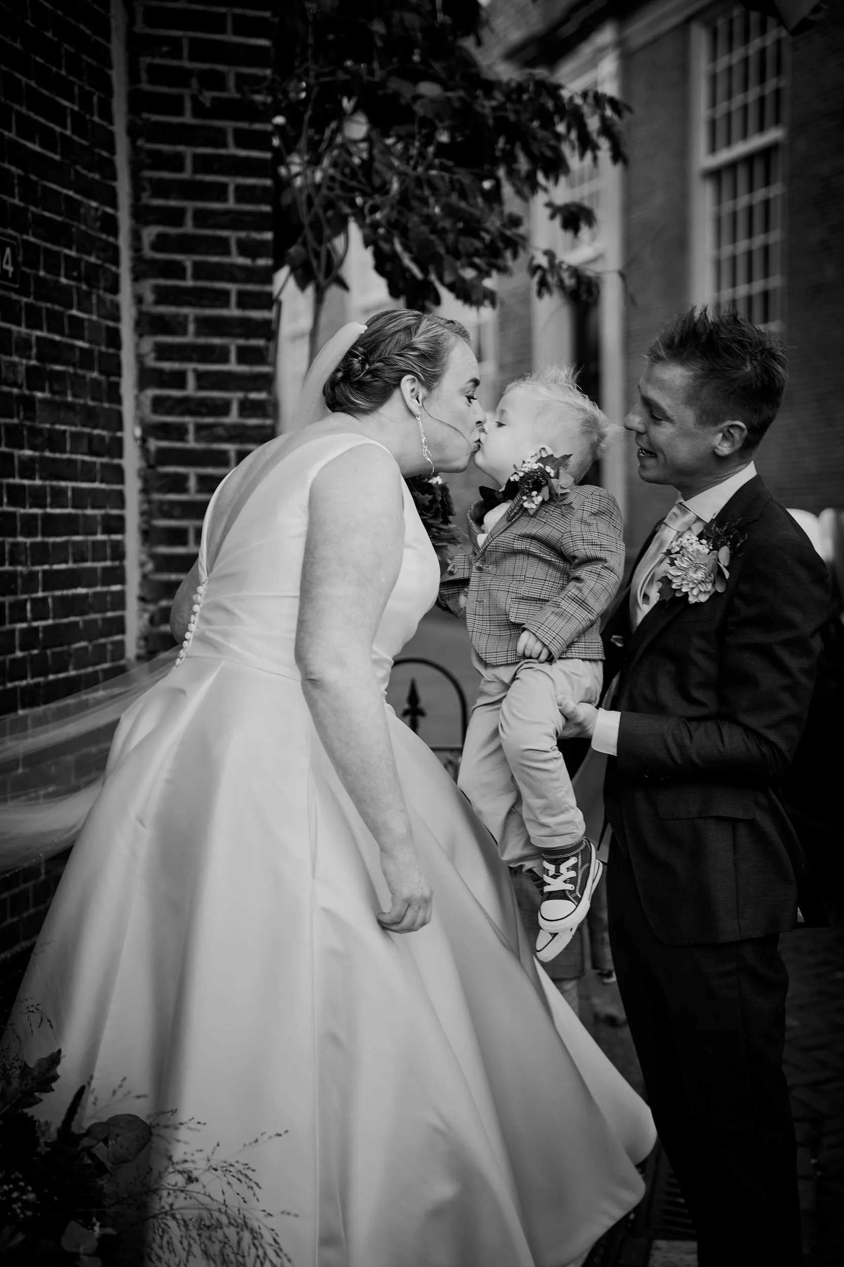 Bruid kust haar kleine zoon terwijl bruidegom toekijkt in de steeg bij Breezze