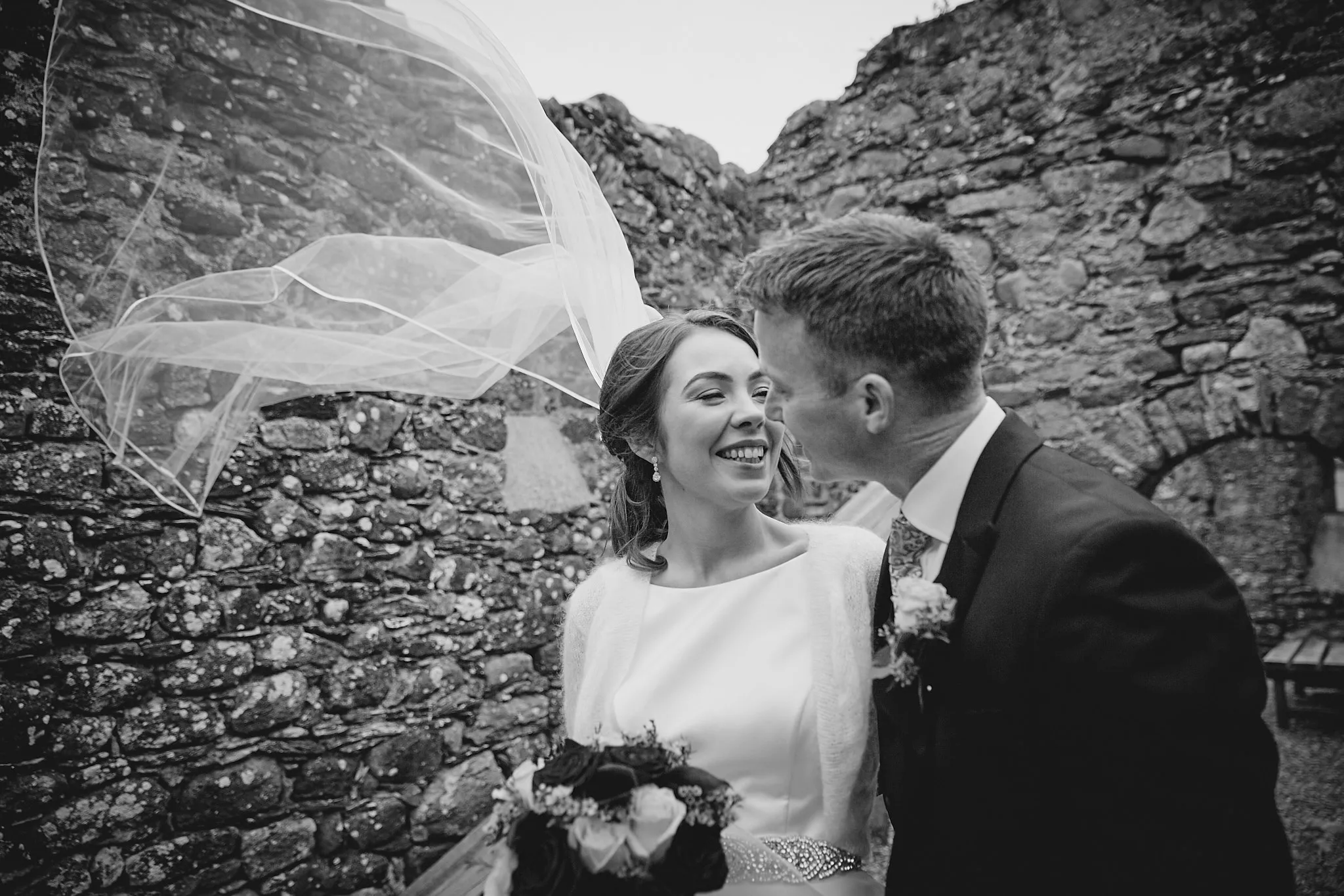 Bruidspaar lacht samen tegen ruwe stenen muur, sluier waait in wind, destination wedding trouwfotografie — Trouwshoot St