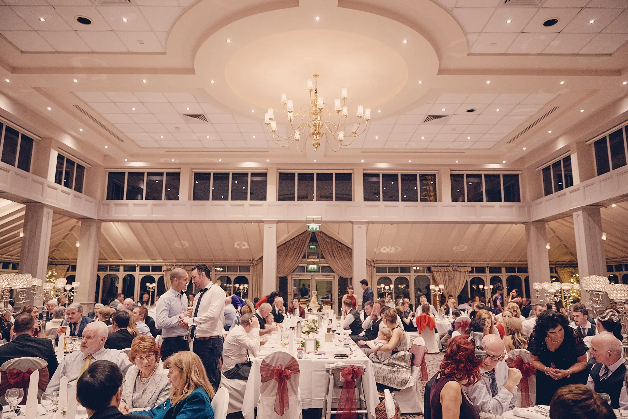 Elegante trouwreceptie in moderne zaal met gasten aan tafels, gouden kroonluchter, destination wedding — Trouwshoot Stef