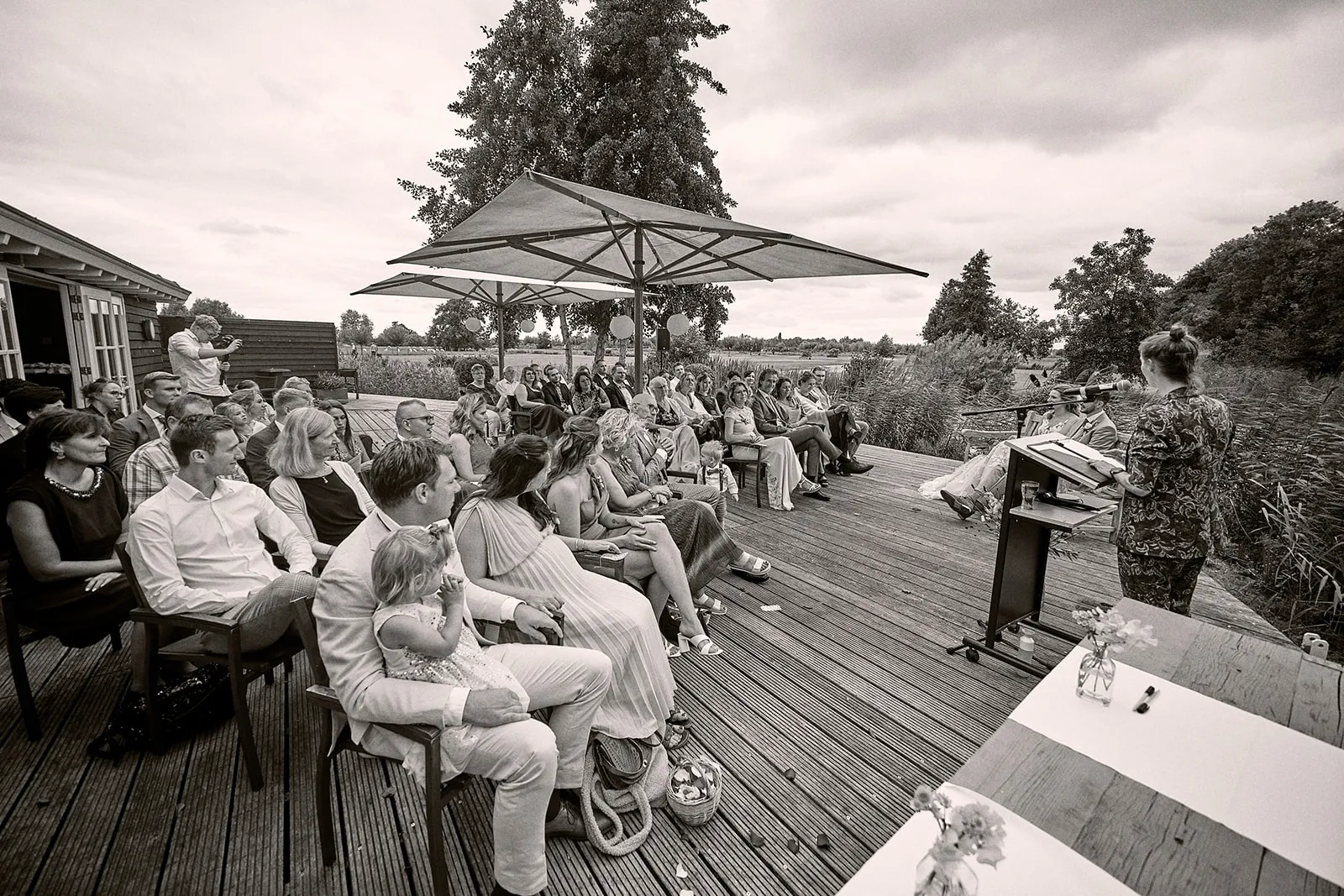 Bruidspaar Milou en Theron ceremonie op houten terras met gasten onder parasols