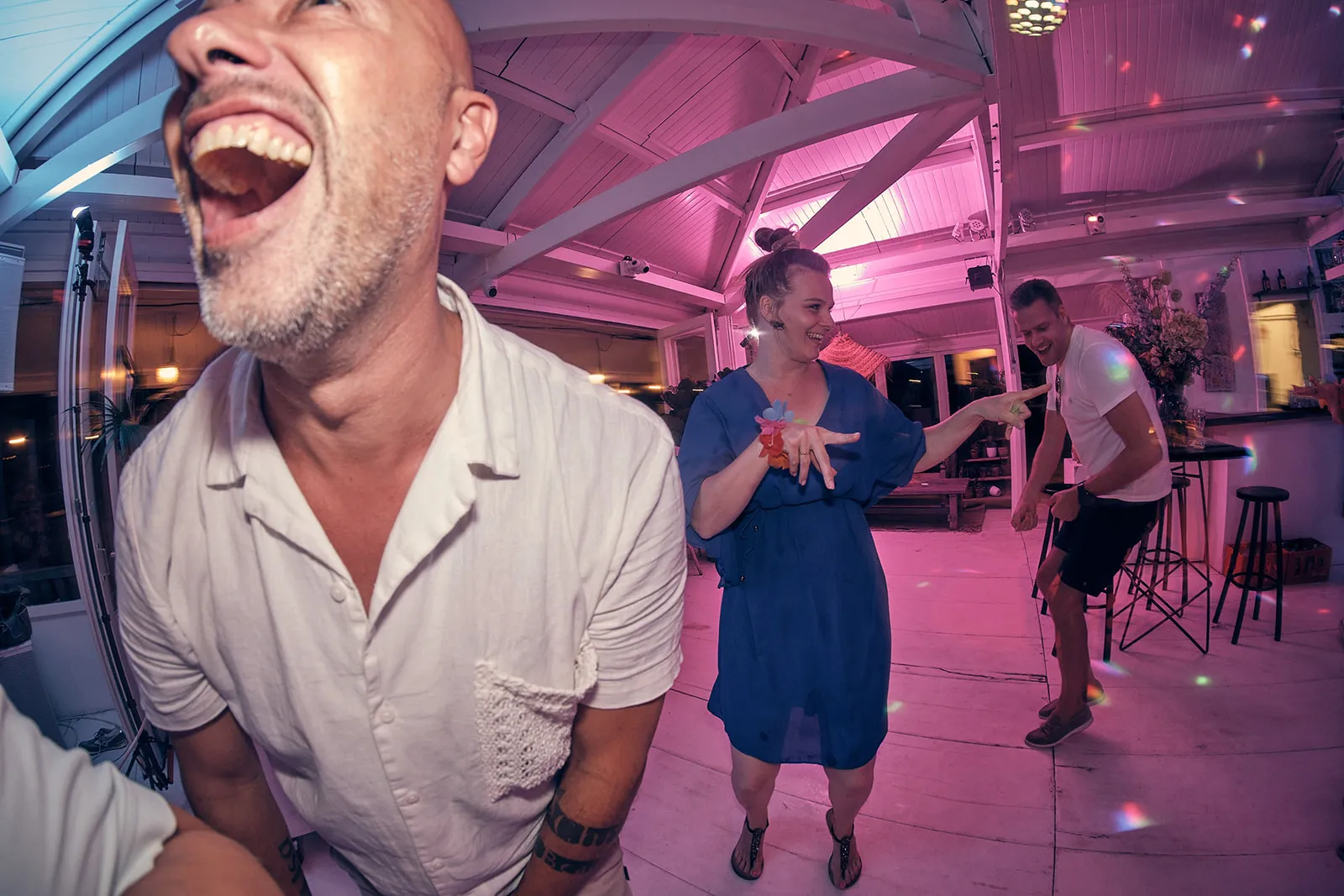 Bruidsgasten dansen uitgelaten in roze verlichting op Strandclub Naturel, festief trouwfeest
