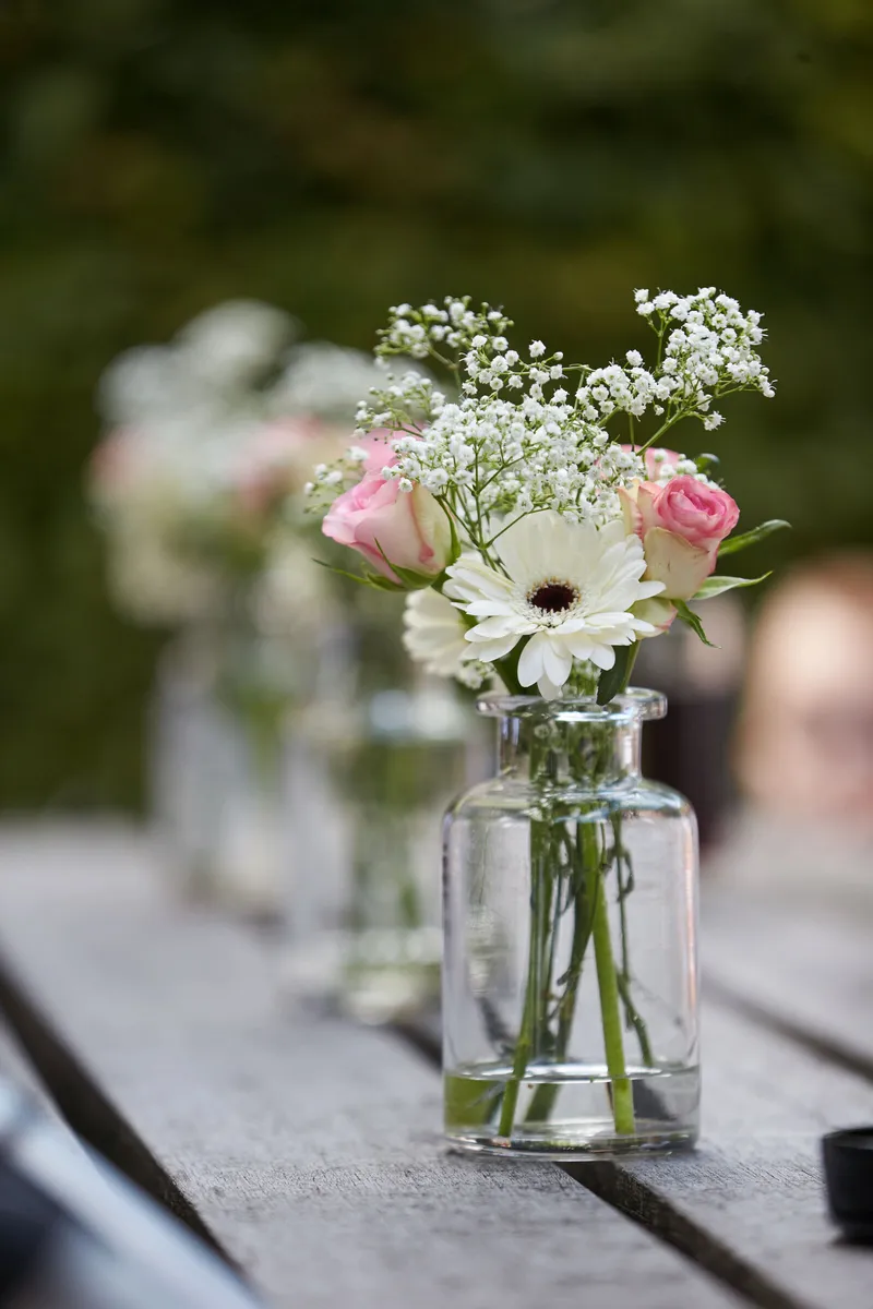 Een vaasje met roze bloemen op tafel