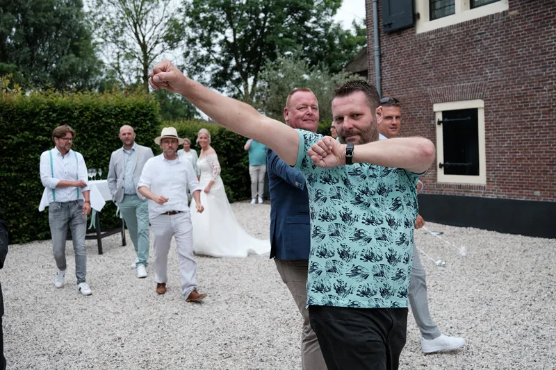 Een gast steekt zijn arm op, Marleen en Eric lopen achter hem over het grind