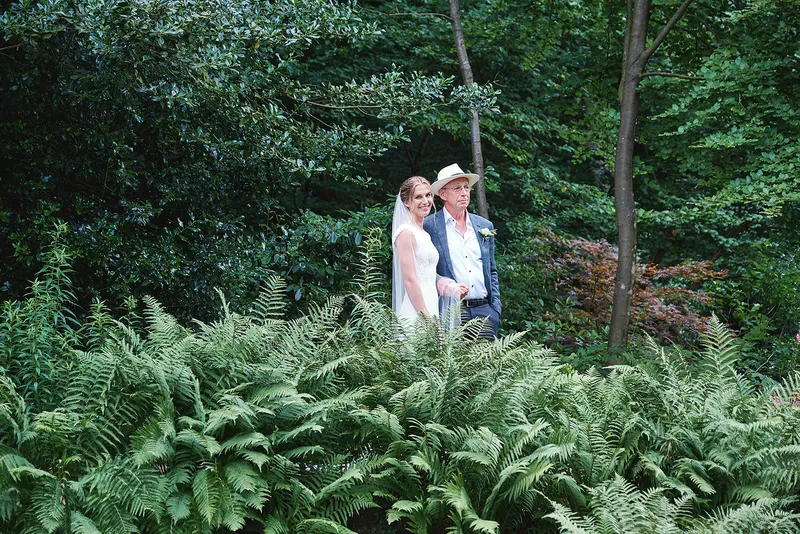 Bruid loopt met haar vader door de varens naar de ceremonie in de tuin
