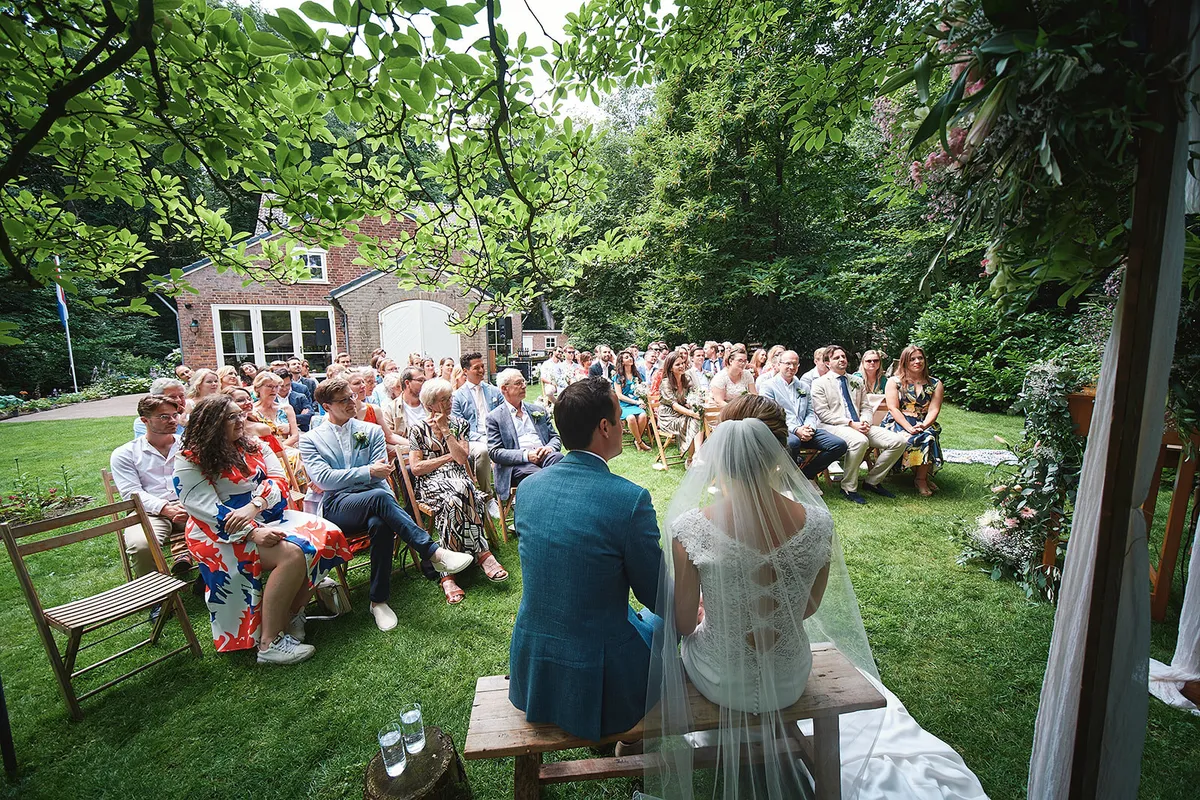 Karien en Niels zitten voor de gasten tijdens de ceremonie in de tuin