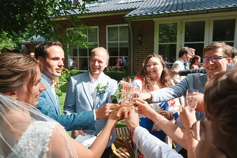 Bruidspaar en gasten proosten met champagne in de tuin