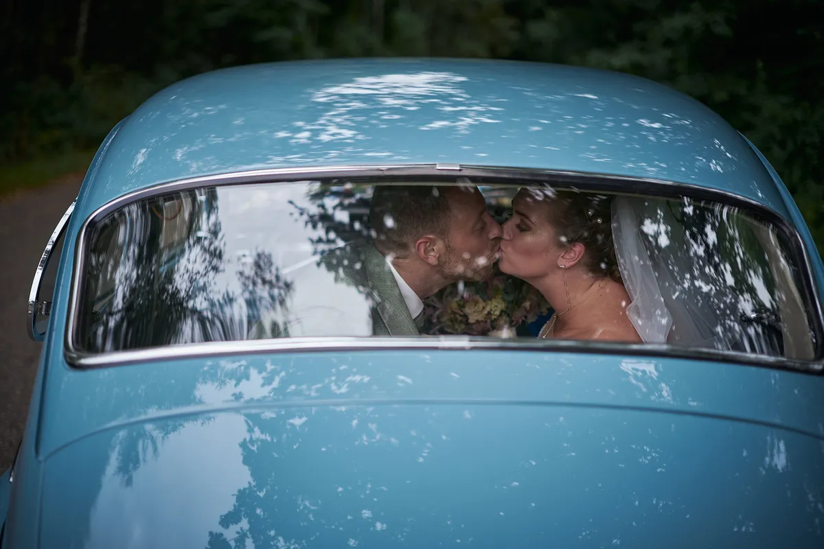 Liëla en Jeffrey kussen door de voorruit van de blauwe oldtimer
