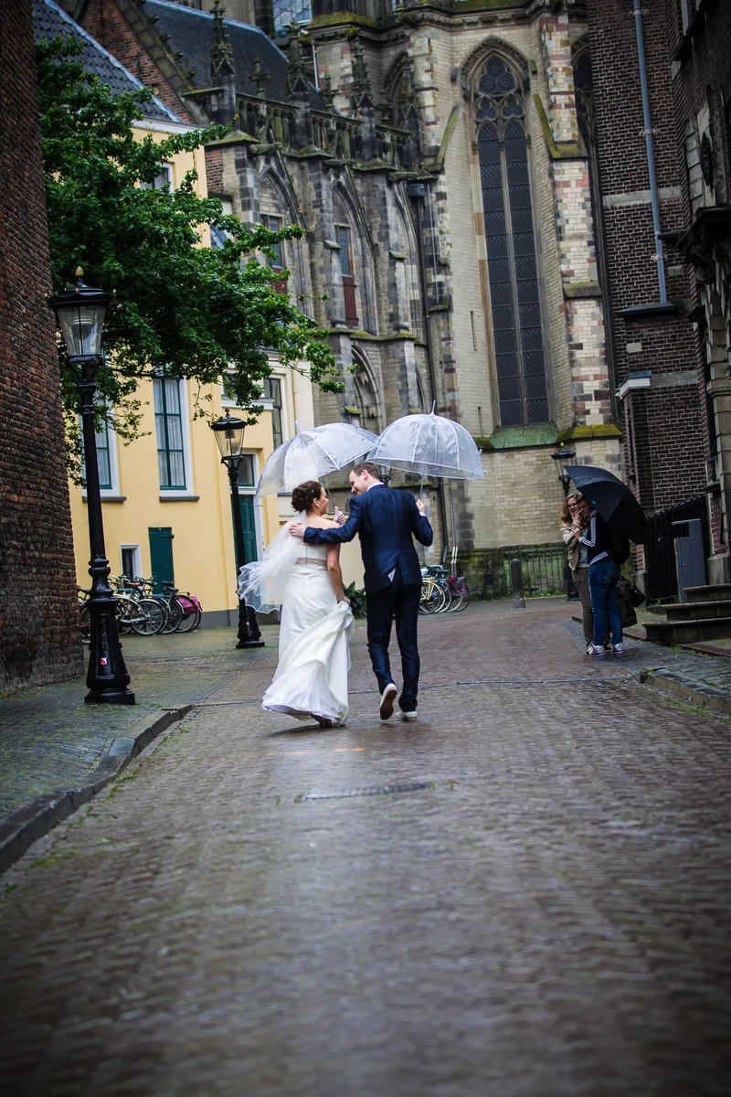 Tessa en Wessel lopen onder een paraplu door de regen, met de kerktoren erachter