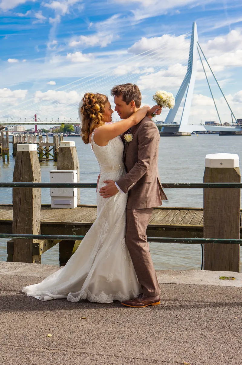 Debora en Joris omarmen elkaar aan de kade, met de Erasmusbrug erachter