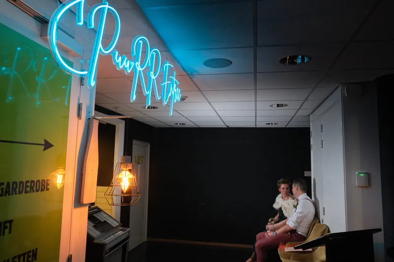 Het neonlogo van Puurr, met Esther en Bart klein in de hoek