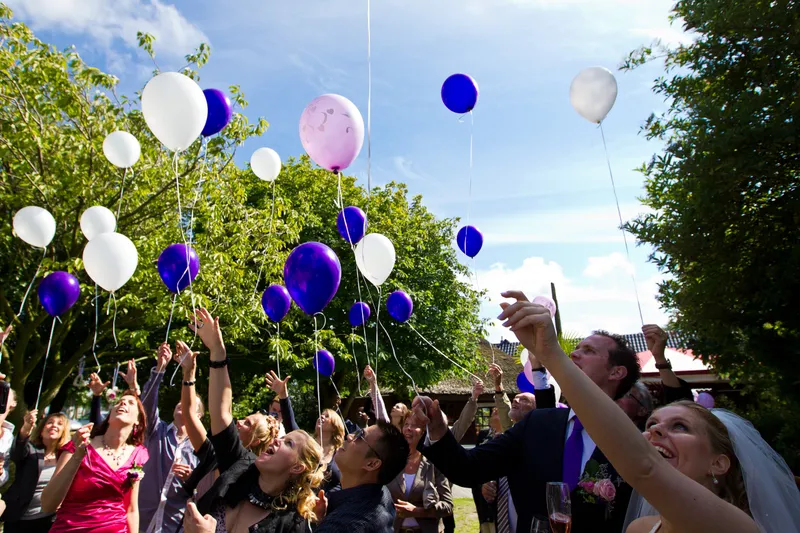 De gasten laten paarse en witte ballonnen los in de tuin van De Viersprong