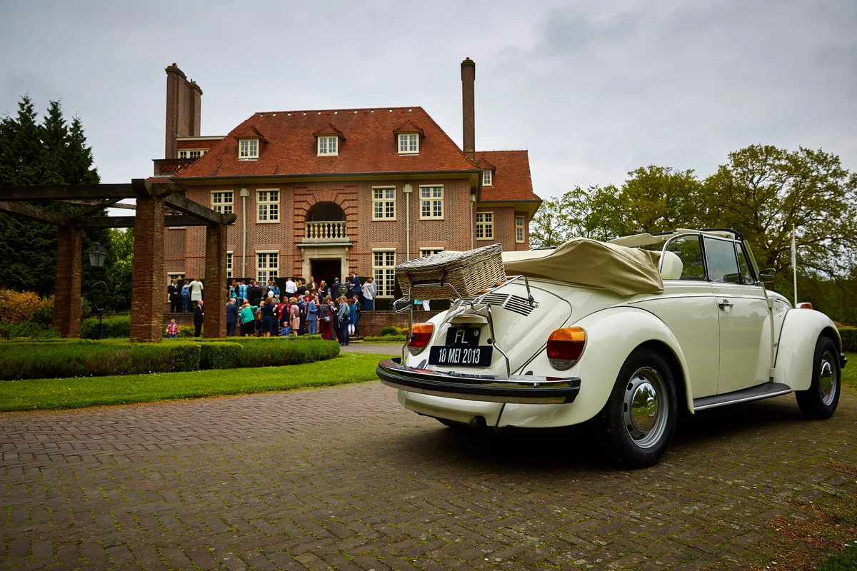 De witte Kever-cabrio voor het landhuis van Voorlinden, met de gasten op de trap