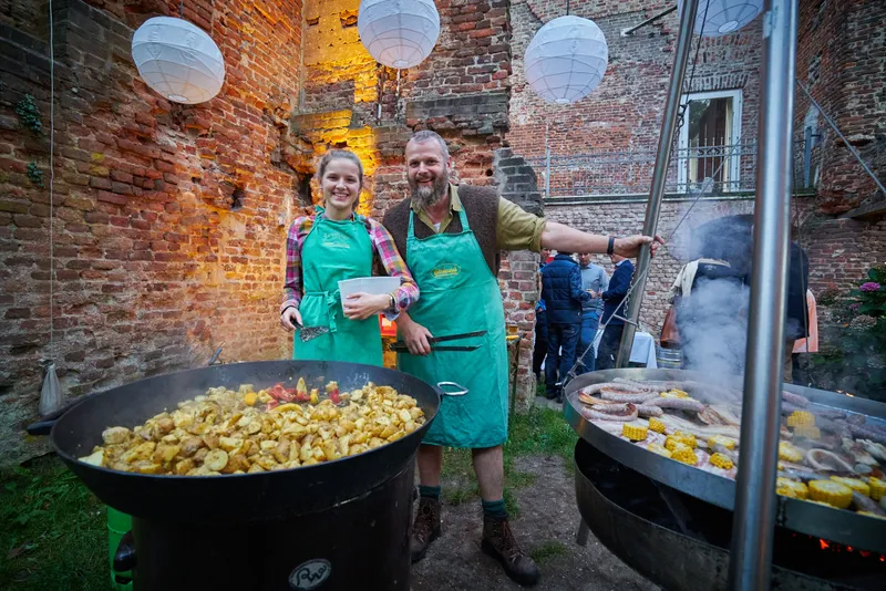 De slager bakt aardappels en worst in grote pannen in de ruïne