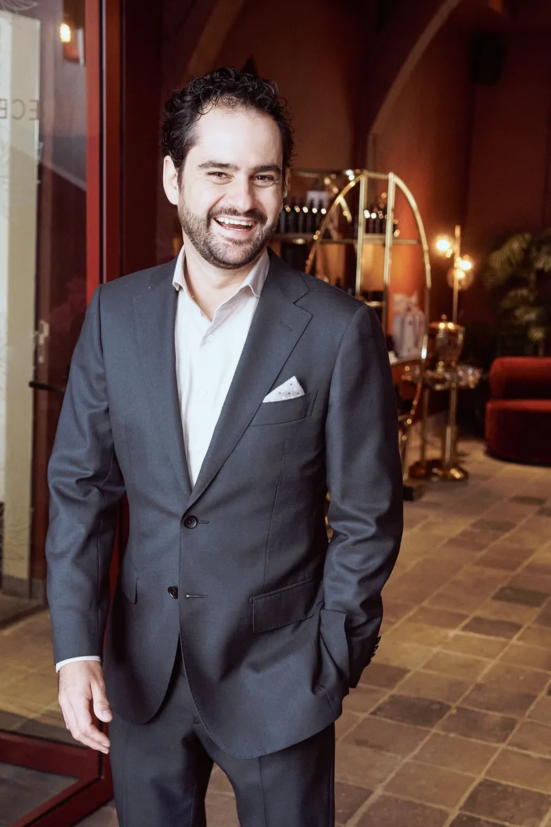 Raphaël lacht in zijn grijze pak in de hal van het hotel