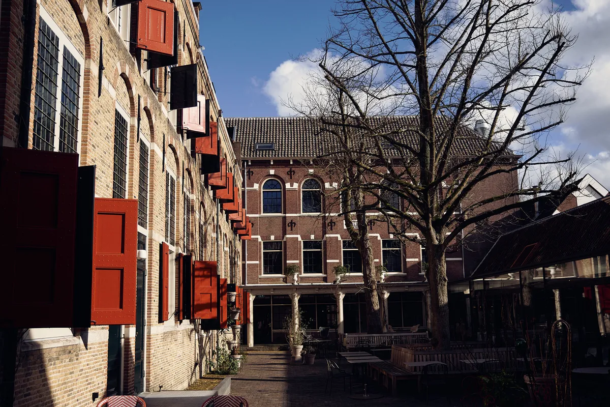 De binnenplaats van Hotel Weeshuis met de rode luiken en een kale boom