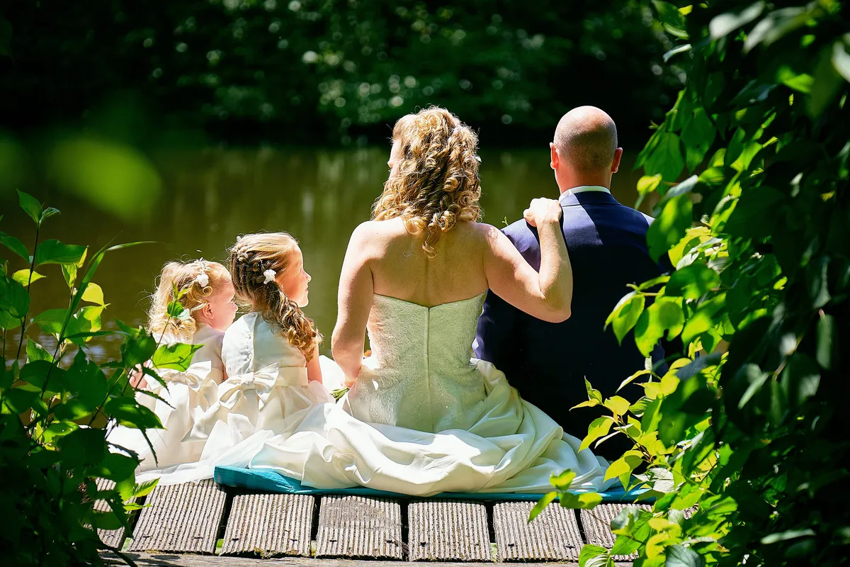 Chantal, Ramon en de meisjes zitten op een steiger aan het water, van achteren