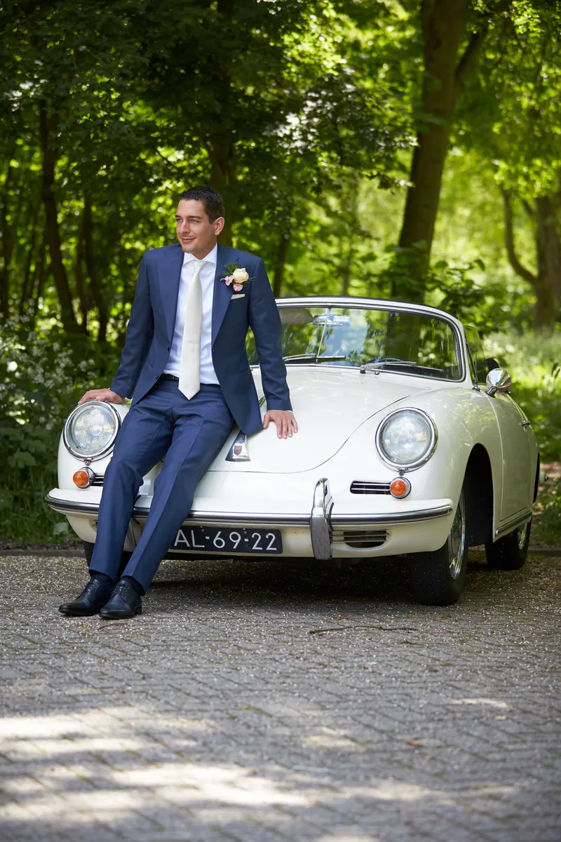 Patrick leunt tegen de witte Porsche onder de bomen