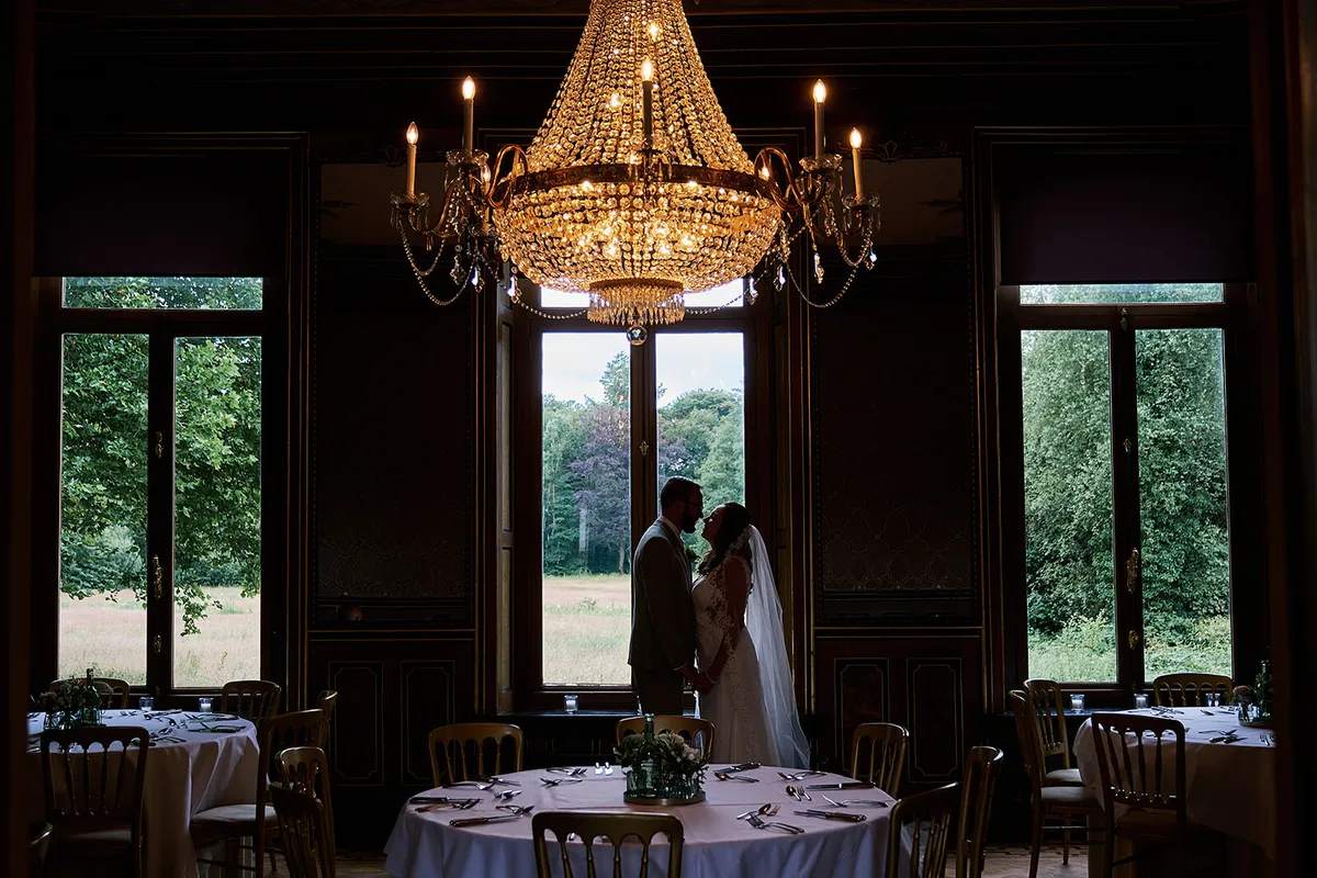 Romana en Sander bij het hoge raam onder een kroonluchter in het landhuis
