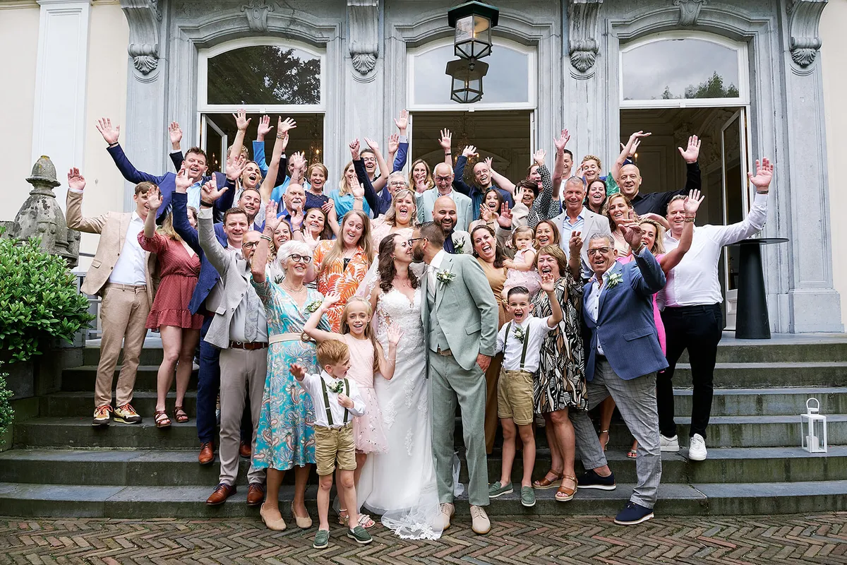 Groepsfoto met alle gasten op de trap van het landhuis, armen in de lucht