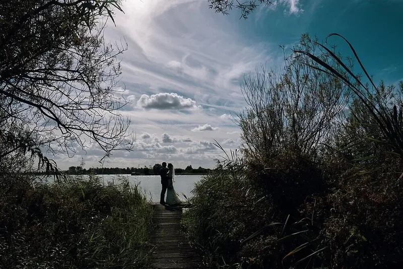 Silhouet van het bruidspaar op een houten vlonder tussen het riet, onder een donkere lucht